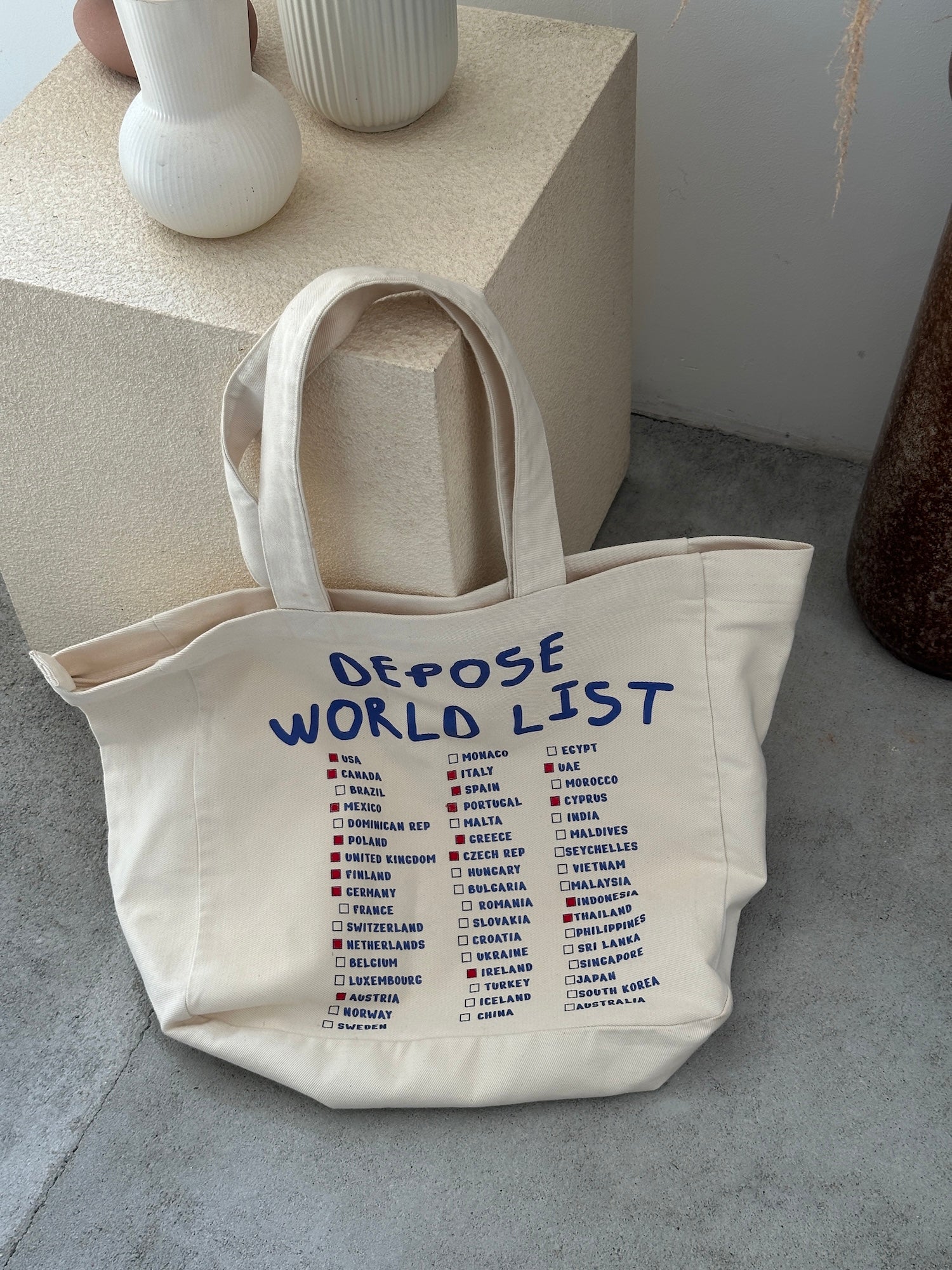 Torba podróżna DEPOSE w kolorze kremowym, zapinana na zamek, z niebieskim napisem WORLD LIST